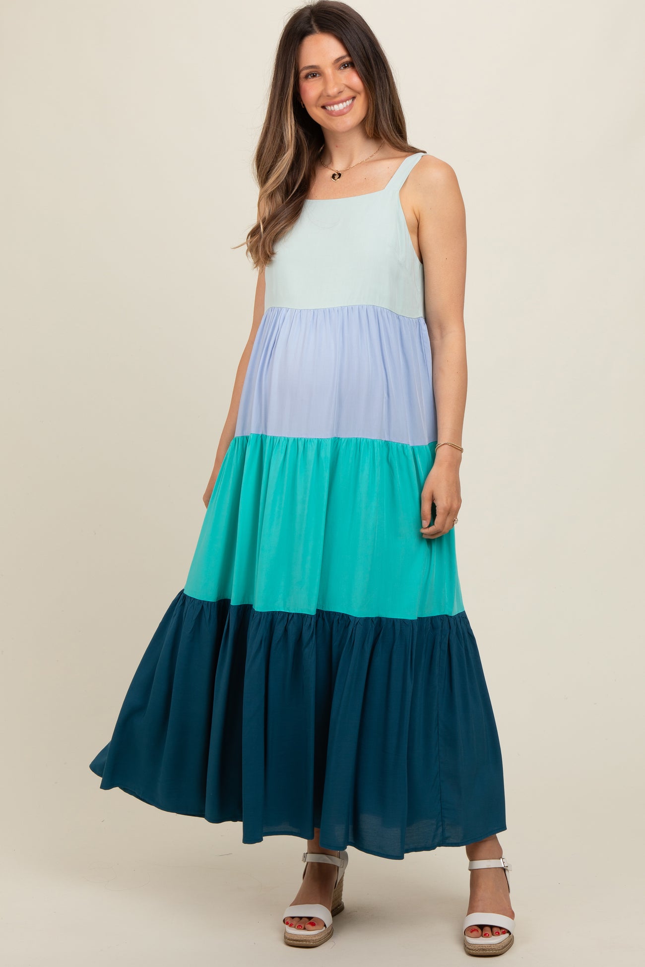 woman wearing a colorful tiered maxi maternity dress in shades of blue and green, showcasing a baby bump