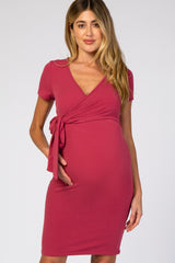 woman wearing a raspberry short sleeve maternity dress with a wrap style and tie detail, holding her baby bump