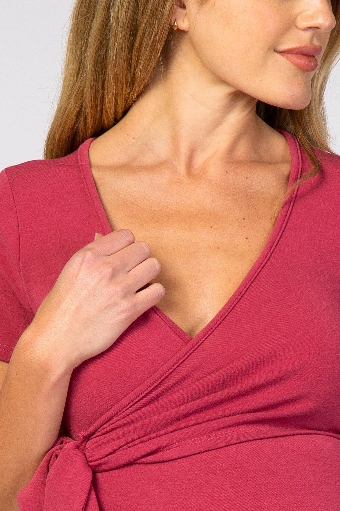 woman wearing a raspberry pink maternity wrap top with short sleeves and a tied detail at the waist
