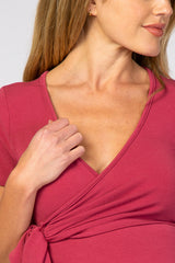 woman wearing a raspberry pink maternity wrap top with short sleeves and a tied detail at the waist