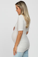 pregnant woman in white short sleeve maternity top and light wash jeans standing in profile against white background
